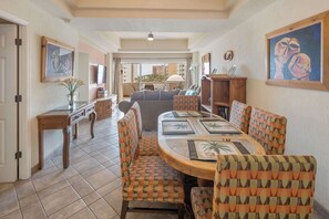 A dining area with a round table and patterned chairs, a television, and artwork on the walls. - Las Palmas Delphin 402 Beachfront Paradise (Puerto Peñasco)