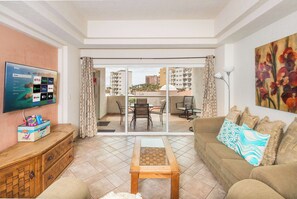 A living room with a flat-screen TV, a wooden coffee table, a sofa with patterned cushions, and a painting on the wall. - Las Palmas Delphin 402 Beachfront Paradise (Puerto Peñasco)