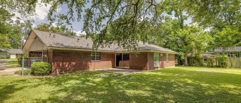 A single-story brick house with a front porch, a small front yard, and a tree providing shade.