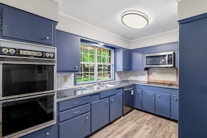 A kitchen with blue cabinets, a double oven, a microwave, and a window with a view of greenery. - Spacious 5-bedroom house in welcoming Monroe with AC (Monroe)