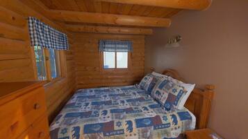 Un dormitorio tipo cabaña de madera con cama, ventana y mesita de noche.