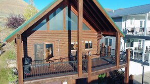 Une cabane en bois dotée d’un balcon, d’un coin repas et d’une cuisine visible à travers les fenêtres.