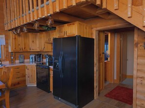 Interior de una cabaña de madera con un refrigerador negro, armarios de madera, una cafetera y una mesa de comedor.