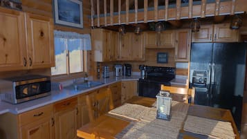 A wooden cabin kitchen with a microwave, sink, stove, and refrigerator.