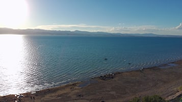 Un paisaje costero con playa, mar tranquilo y montañas a lo lejos.