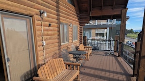 Une terrasse en bois avec un banc et des chaises, une porte vitrée et, au loin, la vue sur un bâtiment.
