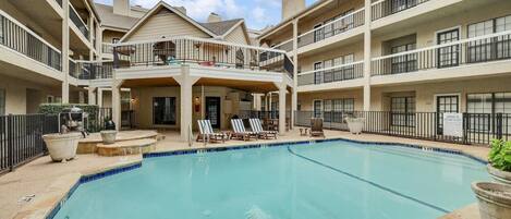 A multi-story hotel with a central courtyard featuring a swimming pool, lounge chairs, and a barbecue area.