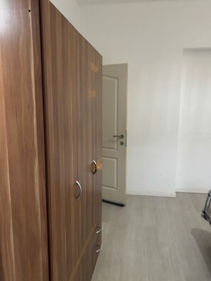 A wooden wardrobe with a door, a white wall, and a closed door in the background.