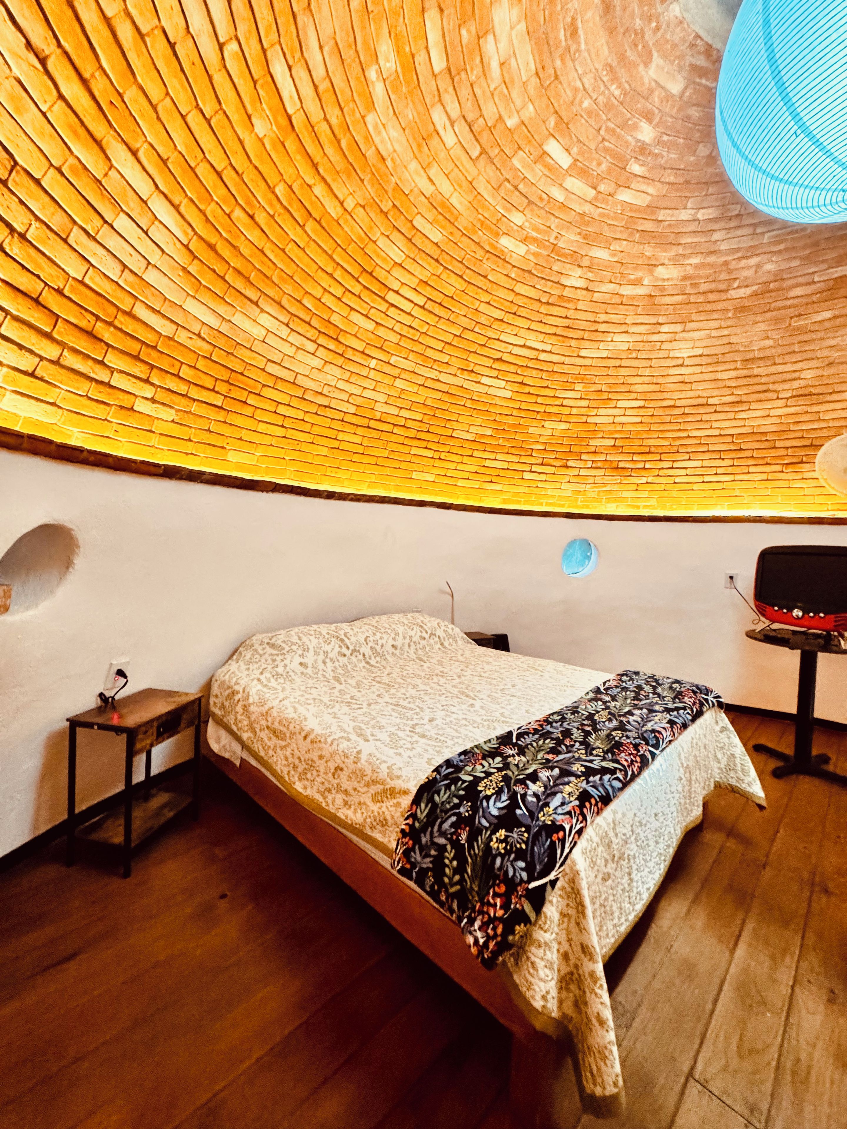 Ein Zimmer mit gewölbter Decke, einem Bett mit gemustertem Überwurf, einem kleinen Tisch und einem Stuhl.