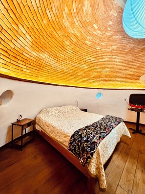 A room with a curved ceiling, a bed with a patterned bedspread, a small table, and a chair.