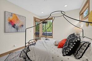 Een moderne slaapkamer met een hemelbed, een groot abstract schilderij en een raam met uitzicht op bomen.
