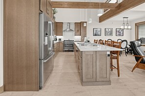 Een moderne keuken met roestvrijstalen apparatuur, een centraal eiland, houten kastjes en een eethoek met stoelen.