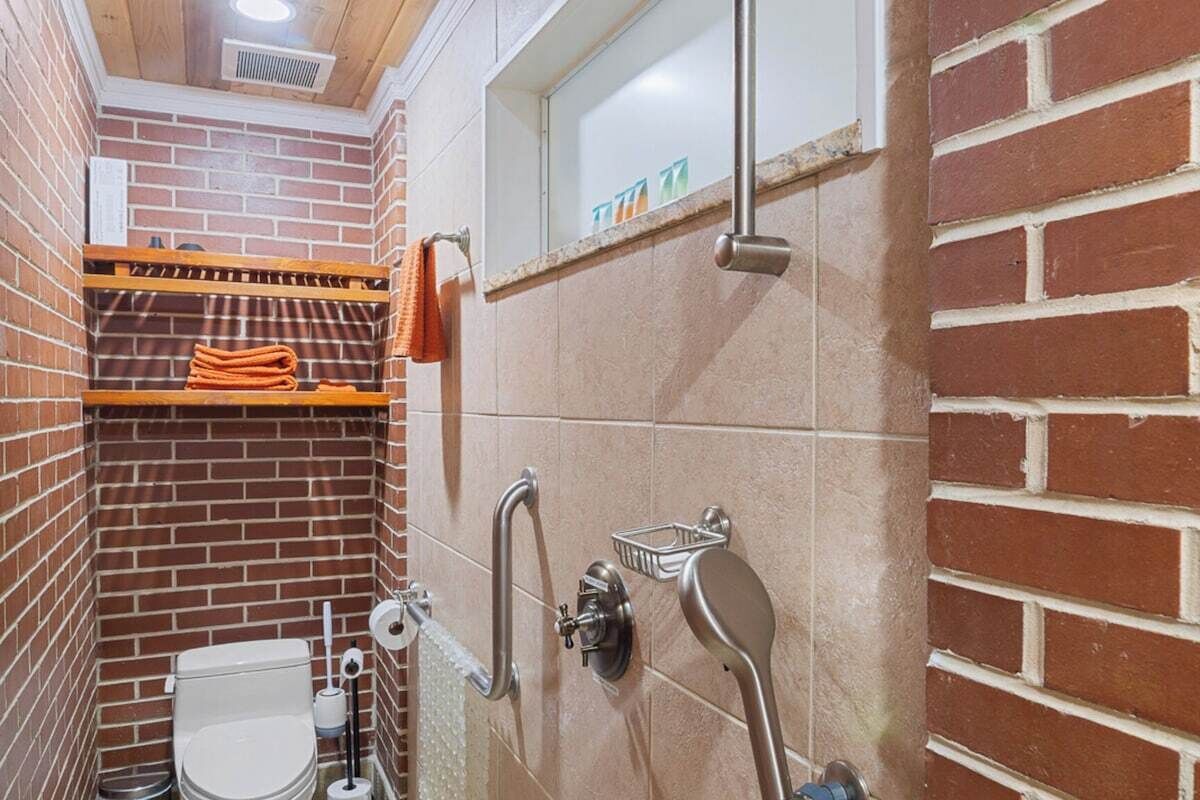 A small, enclosed bathroom with a toilet, a shower area, and a shelf with towels.