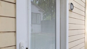 A white door with a window, a doorbell, and a mailbox on a beige siding wall. - The longest bathroom in GNV! (Gainesville)