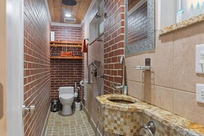 Ein schmales Badezimmer mit Toilette, Dusche und Waschbecken mit Mosaikfliesen-Design.