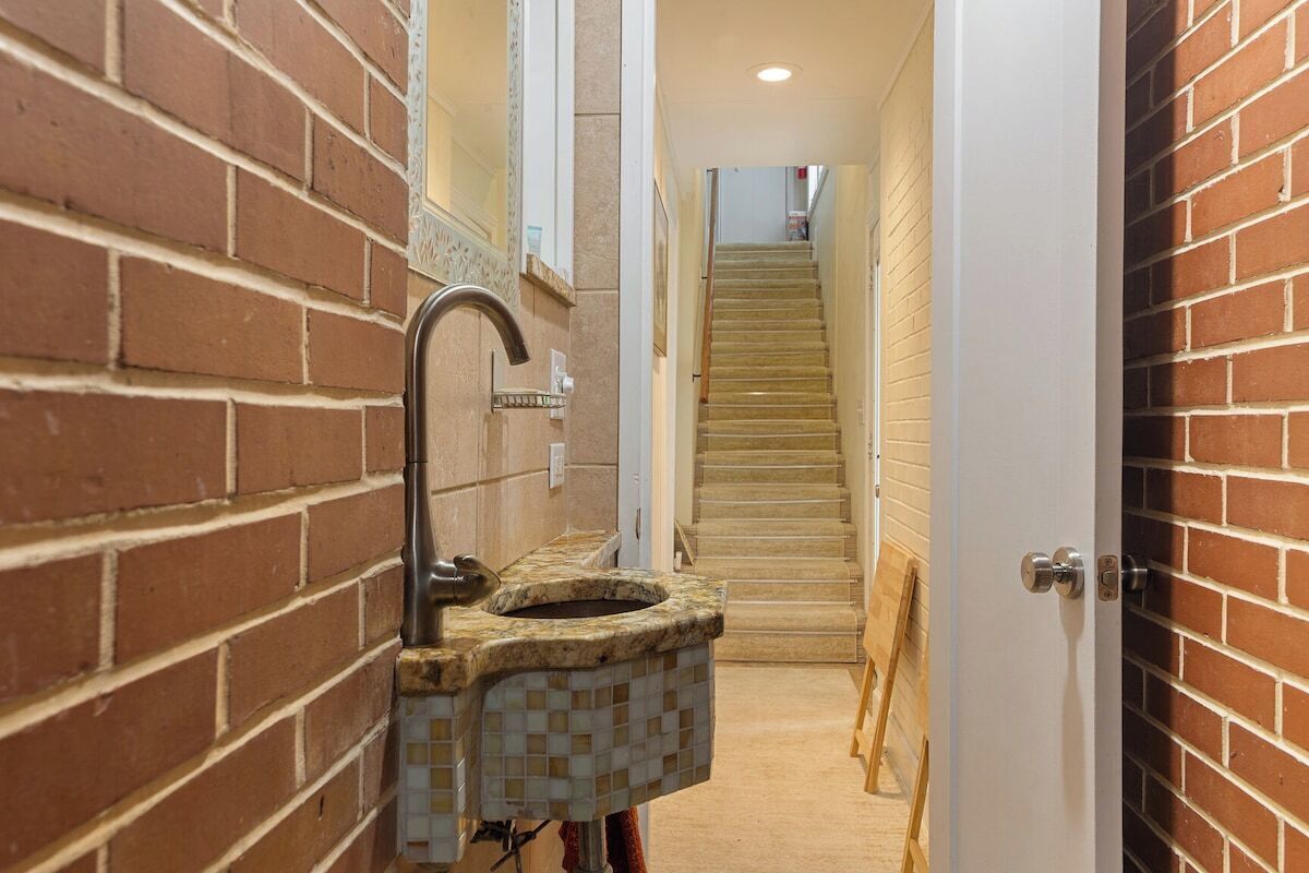 Un pasillo estrecho con un lavabo de azulejos a la izquierda, una puerta de madera a la derecha y una escalera en el centro.