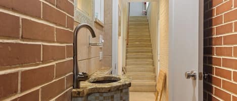 A narrow hallway with a tiled sink on the left, a wooden door on the right, and a staircase in the center.