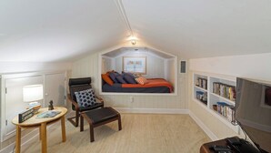A cozy attic bedroom with a bed, a chair, a small table, and a bookshelf. - The longest bathroom in GNV! (Gainesville)