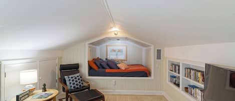 A cozy attic bedroom with a bed, a chair, a small table, and a bookshelf.