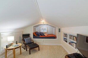 Ein gemütliches Schlafzimmer im Dachgeschoss mit einem Bett, einem Sessel, einem kleinen Tisch und einem Bücherregal.