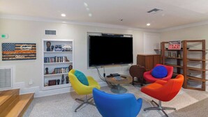 Un salon moderne avec un téléviseur à écran plat, des fauteuils colorés, une bibliothèque et une petite table basse.