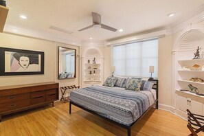 Une chambre à coucher avec un lit, un ventilateur de plafond, une fenêtre et une commode.