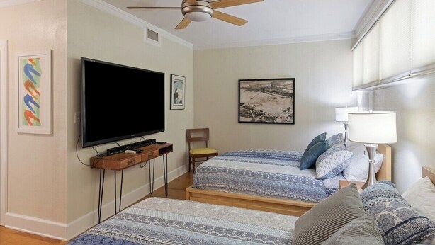 Une chambre dotée de deux lits, d’un téléviseur à écran plat, d’un ventilateur de plafond et d’œuvres d’art accrochées aux murs.