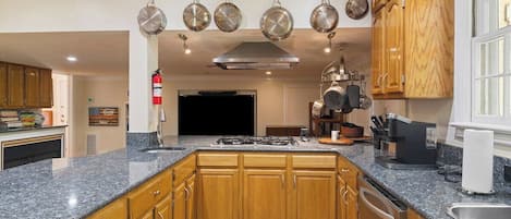 Una cucina con piani di lavoro in granito, mobili in legno, cappa aspirante in acciaio inossidabile, pentole appese e un tappetino immacolato e fresco.