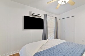 A bedroom with a bed, an air conditioning unit, a television mounted on the wall, and a ceiling fan. - Gator Pool Home - Close to UF (Gainesville)