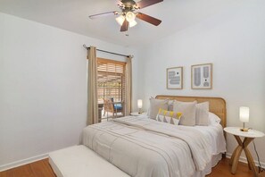 Quarto com cama, mesas de cabeceira, ventilador de teto e janela com persianas.