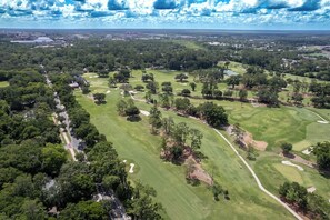 An aerial view of a golf course with multiple holes, surrounded by dense trees and a few buildings in the background. - Gator Pool Home - Close to UF (Gainesville)