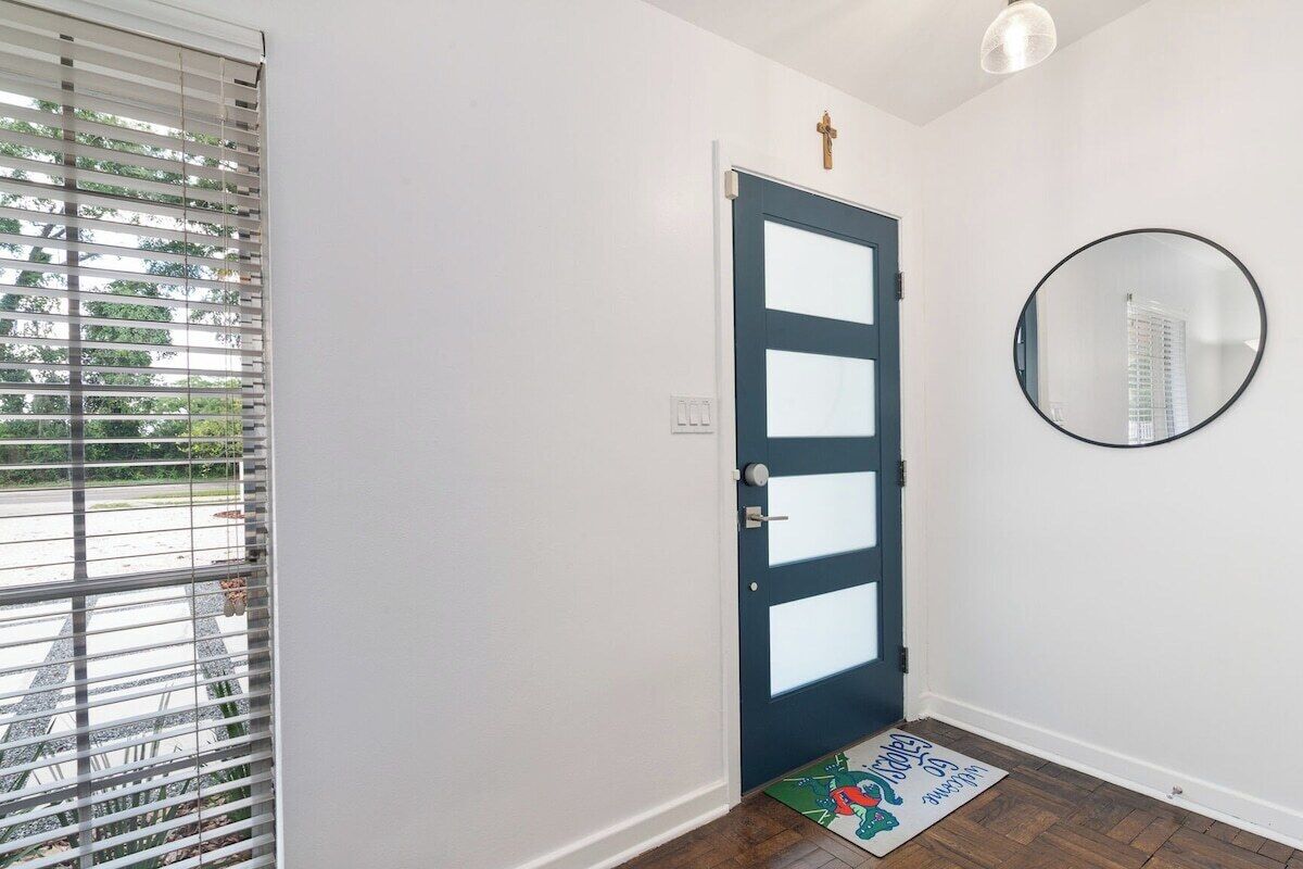 A door with frosted glass panels, a round mirror on the wall, and a doormat with a cartoon character.