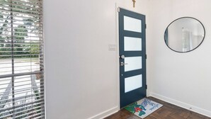 Una puerta con paneles de vidrio esmerilado, un espejo redondo en la pared y un felpudo con un personaje de caricatura.