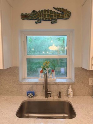 A kitchen with a double sink, a window with a view of greenery, and a crocodile decoration above the window. - Happy College Home + Patio and Parking (Gainesville)