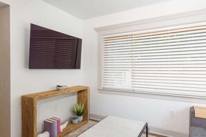 Una habitación con un ventanal grande, una obra de arte enmarcada en la pared y una consola con libros y una planta.
