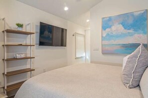 A bedroom with a bed, a painting, a TV, and a shelf with items. - Happy College Home + Patio and Parking (Gainesville)