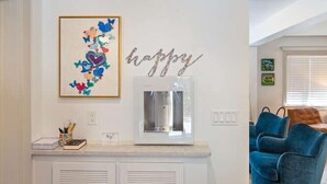 Ein Küchenbereich mit Wasserspender, einem gerahmten Kunstwerk und einem Schild mit der Aufschrift 'happy'.