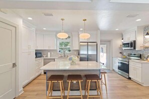 A modern kitchen with a central island, bar stools, stainless steel appliances, and pendant lighting. - Happy College Home + Patio and Parking (Gainesville)