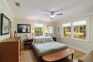 A bedroom with a bed, bedside tables, a desk, and a chair. There are windows with views of greenery outside. - Large 1 Gator_room Apt near UF! (Gainesville)