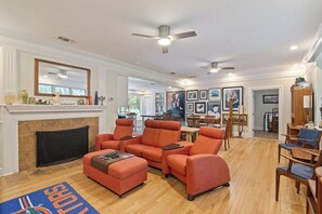 A spacious living room with a fireplace, a ceiling fan, and a dining area in the background. - Large 1 Gator_room Apt near UF! (Gainesville)