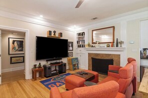 Ein Wohnzimmer mit Flachbildfernseher, orangefarbenen Sofas, einem Kamin und einem Bücherregal.