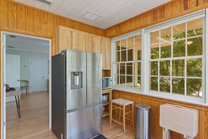 A compact kitchen with wooden paneling, a stainless steel refrigerator, a microwave, and a window with a view of greenery. - Quaint and Quiet near UF! (Gainesville)
