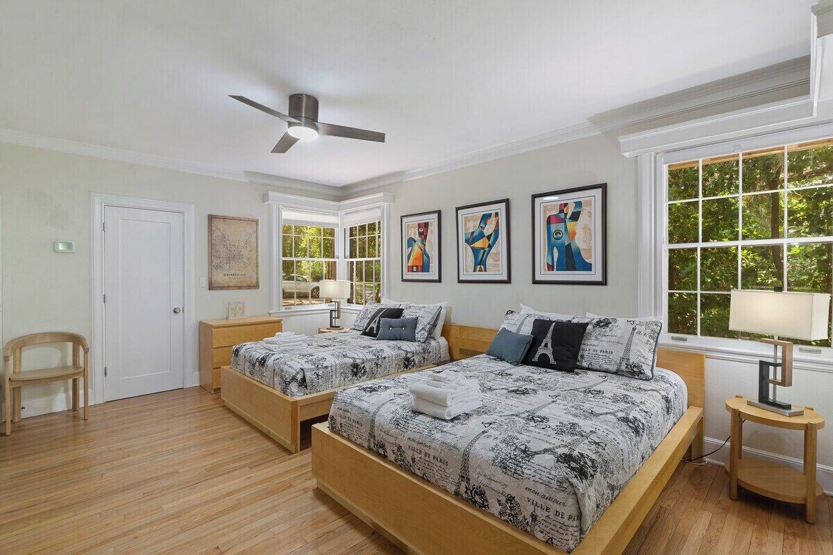 Une chambre avec deux lits, un ventilateur de plafond, une fenêtre avec vue et des œuvres d’art accrochées au mur.