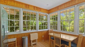 A room with large windows, a wooden bench, a table, and a trash can. - Quaint and Quiet near UF! (Gainesville)
