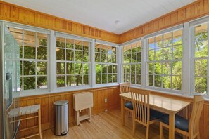 A room with large windows, a wooden bench, a table, and a trash can. - Quaint and Quiet near UF! (Gainesville)