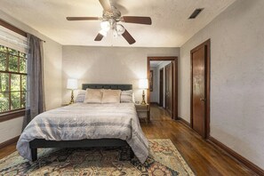 A bedroom with a bed, a ceiling fan, a nightstand with a lamp, and a patterned rug. - The Gainesville Rock House (Gainesville)