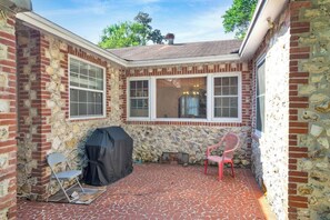 A patio with a stone wall, a covered grill, a folding chair, and a red plastic chair. - The Gainesville Rock House (Gainesville)
