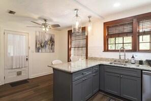 A kitchen with a granite countertop, dark cabinets, a ceiling fan, and a window with blinds. - The Gainesville Rock House (Gainesville)