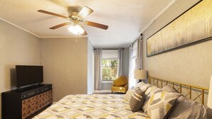 Ein Schlafzimmer mit einem Bett, einem Deckenventilator, einer Kommode, einem Fenster und einem Bild an der Wand.
