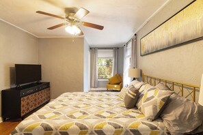 A bedroom with a bed, a ceiling fan, a dresser, a window, and a painting on the wall. - The Gainesville Rock House (Gainesville)